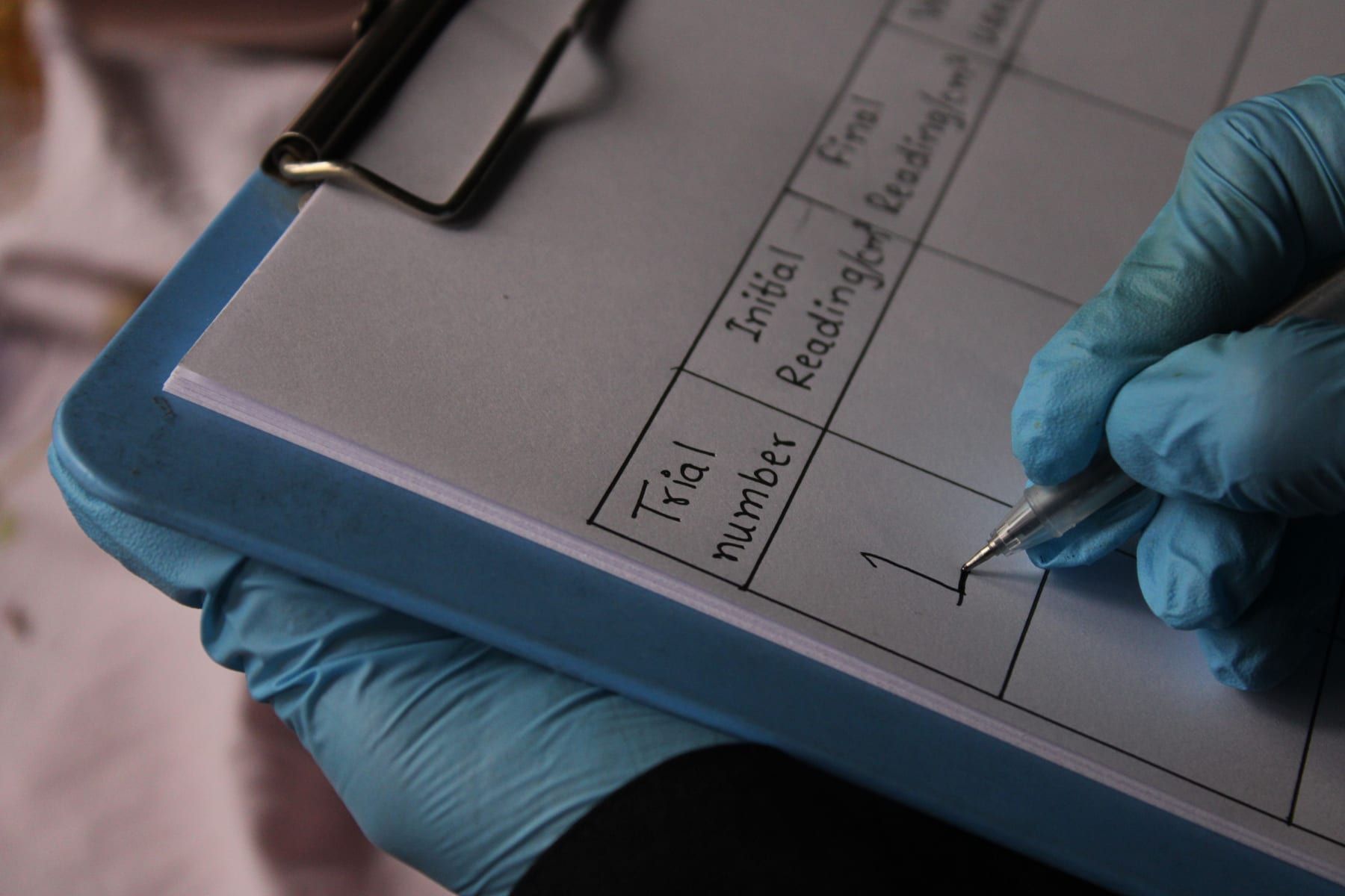 A gloved hand fills in a bench data sheet on a clipboard.